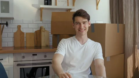 Young man looks in camera and smiles sitting at glass table Stock Footage 201167915