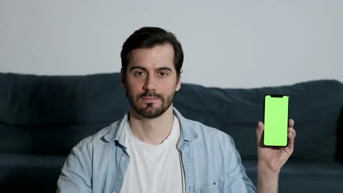 A young Man Looks at the Camera Shows a Smartphone with a Green Screen Stock Footage 144682652