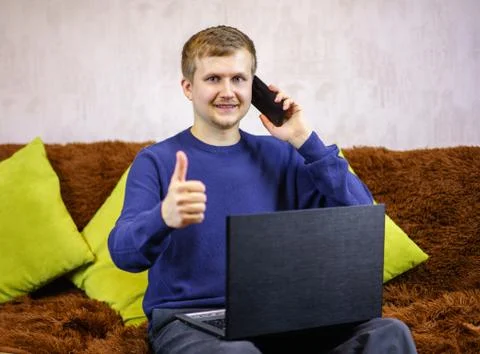 A young man looks at the camera, shows likes, talks on the phone and smiles. Stock Photos