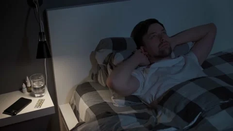 Young man looks at the ceiling at night while lying in bed instead of sleeping Stock Footage 155003749