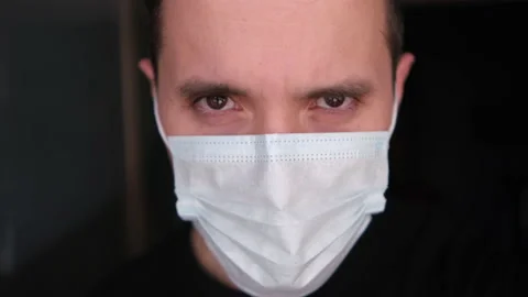 A young man looks evil from under his brows in a protective medical mask, a clos Stock Footage 146834127