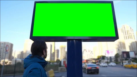 A young man looks green screen billboard on urban, street traffic.Cars are going Vidéo 124159785