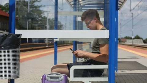Young man looks happy while texting on smartphone and sitting on the train stop Stock Footage 78655116