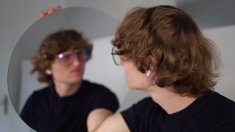 Young man looks at his reflection with playful confusion as if questioning what  Stock Footage 312981815