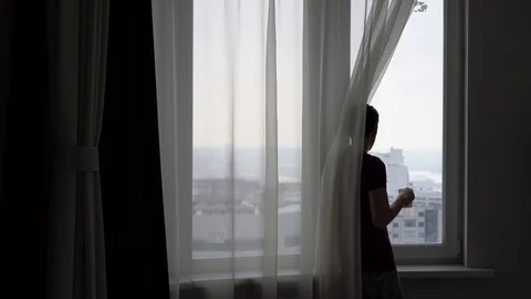 Young man looks out the window at the city and drinks tea or coffee 库存影片 87708989