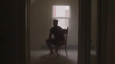 Young Man Looks Out Window While Sitting Alone In Bedroom Vidéo 208711944