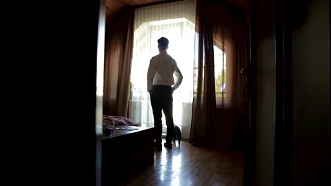 A young man looks out the window, a black cat sits on the side Stock Footage 252757149