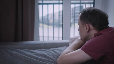 A young man looks out the window, watching the movement outside, leaning on the Stock Footage 329918156