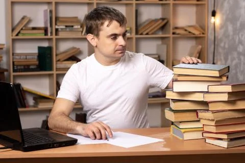 Young man looks at a stack of books on the background of a bookcase. Foto stock