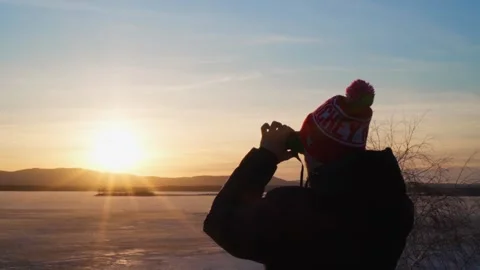 A young man looks through binoculars at a frozen lake and mountains at sunset. Stock Footage 238527045