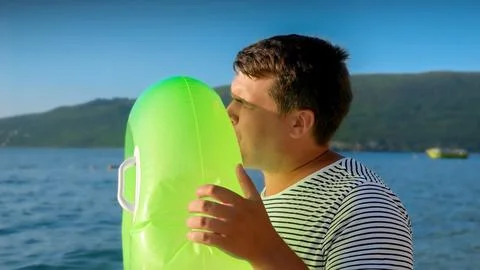 Young man lovingly inflates an inflatable swimming ring for his kids on a sun Foto stock