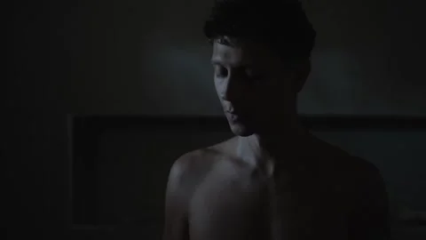 Young man lowers head from side profile to bowed pose in dim interior, cool rim Stock-Footage 347302701