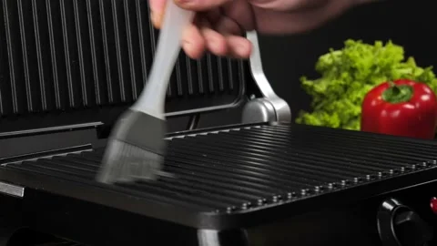 Young man lubricates the surface of a home electric grill Stock Footage 239071580