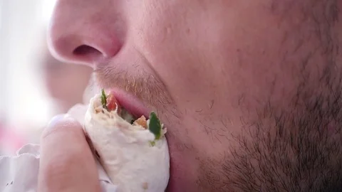 A young man, at lunch bites off a delicious juicy shawarma, close-up. slow Stock Footage 78536791