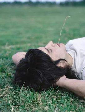 Young man lying on back with hands behind head and piece of grass in mouth Stock Photos
