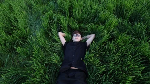 A young man lying in a beautiful field of green grass. Video stock 274159890