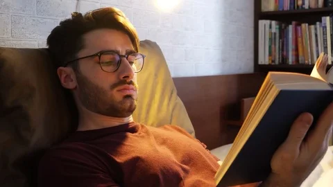 Young man lying in bed and reading a book Stock Footage 79662411