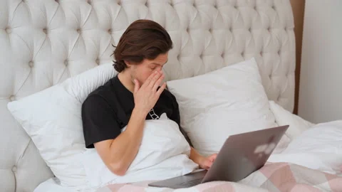 Young man lying in the bed and trying to work on the laptop, tired and nod off Stock Footage 138117843