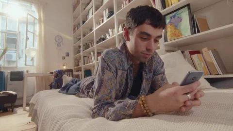 Young Man Lying on Bed and Messaging on Phone at Home Stock Footage 243227959