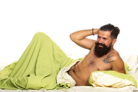 Young man is lying on bed and enjoying the morning. Attractive bearded guy Stock Photos
