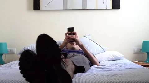 Young man lying on a bed in a bright room using a cell phone. Stock Footage 164721894
