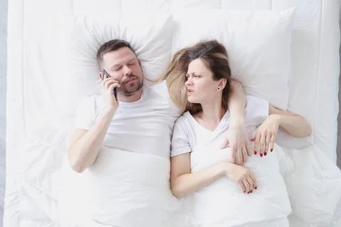 Young man lying in bed with his wife and talking on cell phone top view Stock Photos