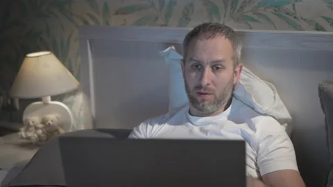 Young man lying in the bed with laptop before sleeping Stock Footage 161908242