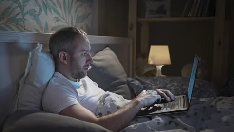 Young man lying in the bed with laptop before sleeping Stock Footage 162490067