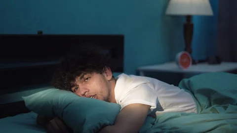 Young man lying in bed late at night trying to sleep suffering insomnia and Vidéo 243793168