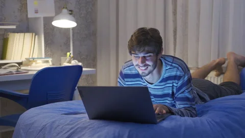 Young man lying in bed looking at laptop. Video stock 222558644