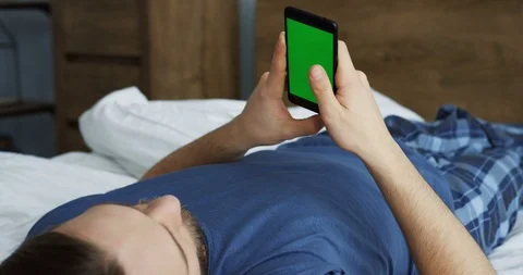Young man lying in the bed in the morning, scrolling and taping on the black 스톡 동영상 88991096