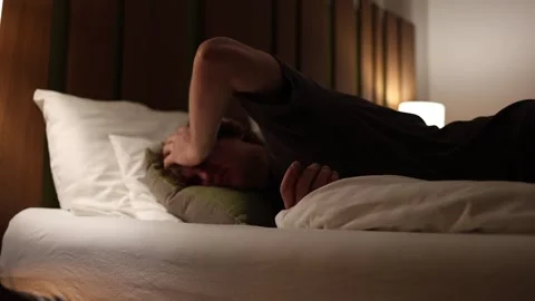 Young man lying in bed at night holding his head in pain suffering from headache Stock Footage 318778716