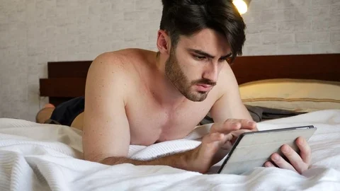 Young man lying in bed using tablet computer Stock Footage