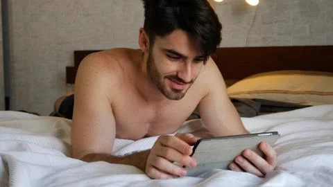 Young man lying in bed using tablet computer Stock Photos