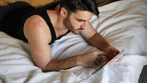 Young man lying in bed using tablet computer Stock Photos