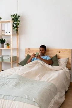 Young man lying in bed using mobile phone. Foto stock