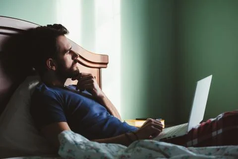 Young man lying in the bed working on a laptop Stock Photos