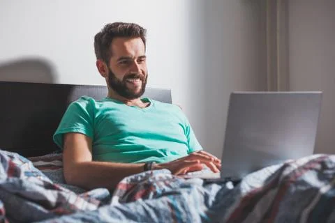 Young man lying in the bed working on a laptop Stock Photos