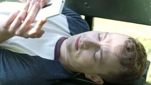 Young man lying on the bench and texting on smartphone, steadycam shot Video stock 76384909