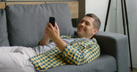Young man lying on couch, browsing in smartphone Stock Footage 113615001