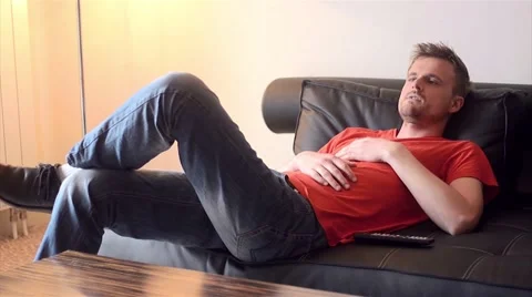 Young man lying on the couch flipping through channels Stock Footage 54273771