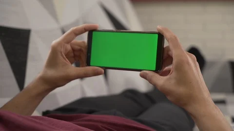 Young man lying on the couch staring at his cell phone, green screen Stock-Footage 129560521