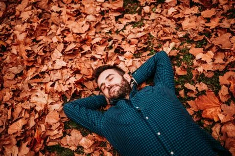 Young man lying down on the ground covered in autumn leaves Stock Photos