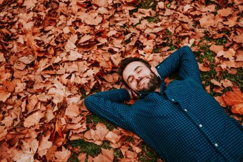 Young man lying down on the ground covered in autumn leaves Stock Photos