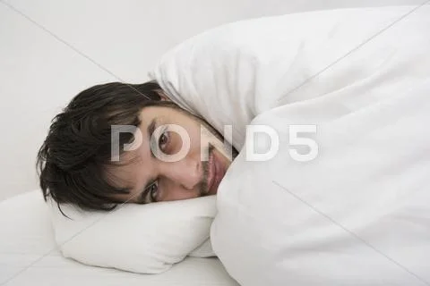 Young man lying down wrapped in duvet Stock Photos