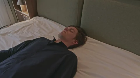 Young man lying dressed in clothes on a bed unconscious or sleeping exhausted Stock Footage 274409136