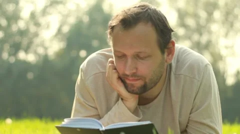 Young man lying on the grass and reading book, dolly shot Stock Footage 8579727