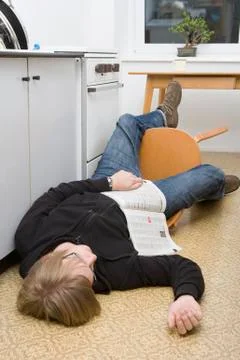Young man lying on the ground with magazine after falling back in a chair Stock Photos