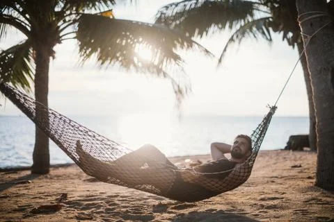 A young man is lying in a hammock at sunset by the ocean. Stockfoto's