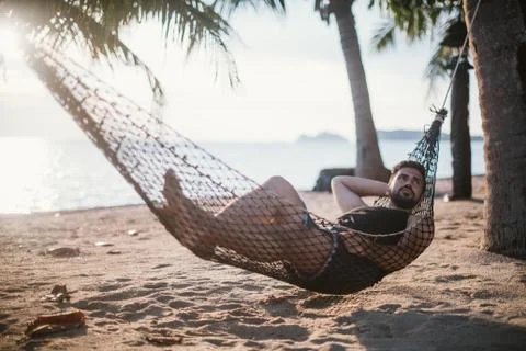 A young man is lying in a hammock at sunset by the ocean. Stock Photos